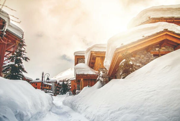 Taken from street. Color photography of several common wooden chalet and fresh snow footpath in french ski resort of Val d'Isere during a beautiful sunny day in january. This image was taken in winter season in Val d'Isere, a french famous ski resort village in Tarentaise mountains, in Savoie, Auvergne-Rhone-Alpes region in European Alps.